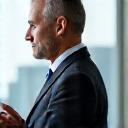Headshot of a strategic business solutions expert, mid-40s, thoughtful and experienced, in a modern office environment. Professional attire.